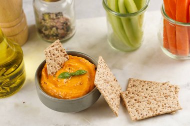 Kırmızı biber sosu portakallı kabak püresi gibi görünüyor, susam tohumlu ince krakerler, uzun şeritler ve mermer tahta üzerinde çubuklarla kesilmiş havuç ve salatalık.