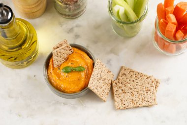 Kırmızı biber sosu portakallı kabak püresi gibi görünüyor, susam tohumlu ince krakerler, uzun şeritler ve mermer tahta üzerinde çubuklarla kesilmiş havuç ve salatalık.