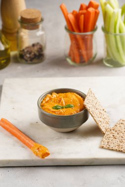 Kırmızı biber sosu portakallı kabak püresi gibi görünüyor, susam tohumlu ince krakerler, uzun şeritler ve mermer tahta üzerinde çubuklarla kesilmiş havuç ve salatalık.