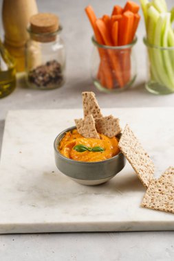 Kırmızı biber sosu portakallı kabak püresi gibi görünüyor, susam tohumlu ince krakerler, uzun şeritler ve mermer tahta üzerinde çubuklarla kesilmiş havuç ve salatalık.