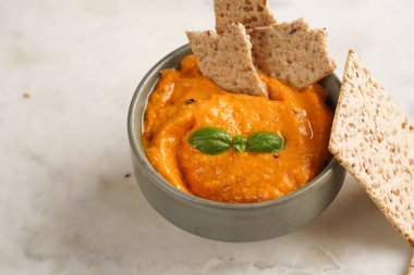 Kırmızı biber sosu portakallı kabak püresi gibi görünüyor, susam tohumlu ince krakerler, uzun şeritler ve mermer tahta üzerinde çubuklarla kesilmiş havuç ve salatalık.