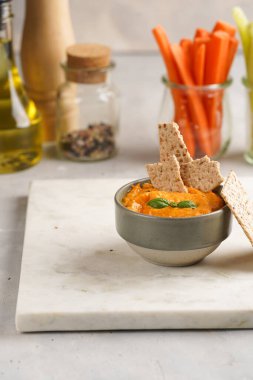 Kırmızı biber sosu portakallı kabak püresi gibi görünüyor, susam tohumlu ince krakerler, uzun şeritler ve mermer tahta üzerinde çubuklarla kesilmiş havuç ve salatalık.