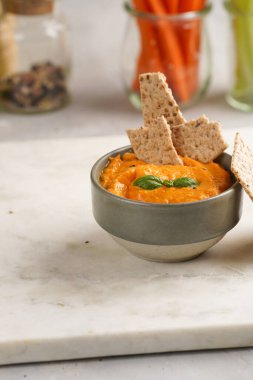 Kırmızı biber sosu portakallı kabak püresi gibi görünüyor, susam tohumlu ince krakerler, uzun şeritler ve mermer tahta üzerinde çubuklarla kesilmiş havuç ve salatalık.