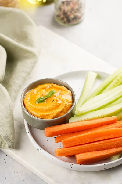 Paprika bell-pepper hummus dip looking like orange pumpkin puree and carrot and cucumber cut in long strips and sticks on a round plate