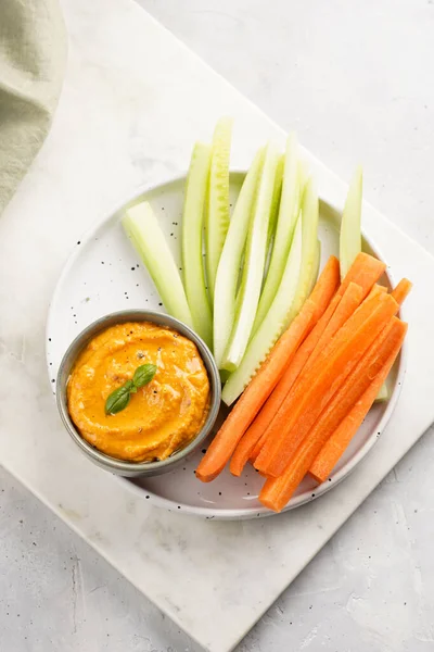 Paprika bell-pepper hummus dip looking like orange pumpkin puree and carrot and cucumber cut in long strips and sticks on a round plate