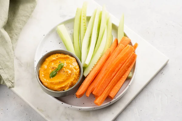 Paprika bell-pepper hummus dip looking like orange pumpkin puree and carrot and cucumber cut in long strips and sticks on a round plate
