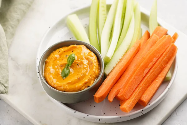 Paprika bell-pepper hummus dip looking like orange pumpkin puree and carrot and cucumber cut in long strips and sticks on a round plate