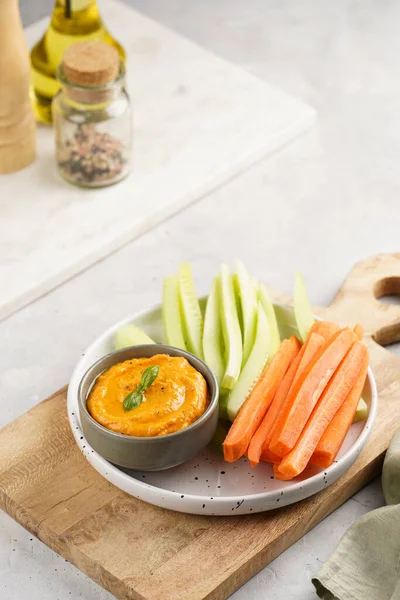 Paprika bell-pepper hummus dip looking like orange pumpkin puree and carrot and cucumber cut in long strips and sticks on a round plate