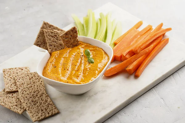Kırmızı biber sosu portakallı kabak püresi gibi görünüyor, susam tohumlu ince krakerler, uzun şeritler ve mermer tahta üzerinde çubuklarla kesilmiş havuç ve salatalık.