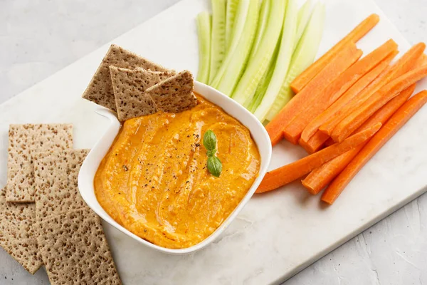 Kırmızı biber sosu portakallı kabak püresi gibi görünüyor, susam tohumlu ince krakerler, uzun şeritler ve mermer tahta üzerinde çubuklarla kesilmiş havuç ve salatalık.