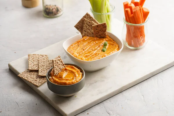 Kırmızı biber sosu portakallı kabak püresi gibi görünüyor, susam tohumlu ince krakerler, uzun şeritler ve mermer tahta üzerinde çubuklarla kesilmiş havuç ve salatalık.