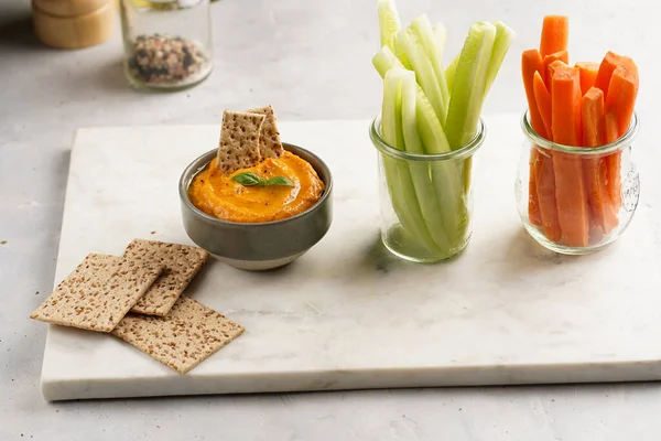 Kırmızı biber sosu portakallı kabak püresi gibi görünüyor, susam tohumlu ince krakerler, uzun şeritler ve mermer tahta üzerinde çubuklarla kesilmiş havuç ve salatalık.