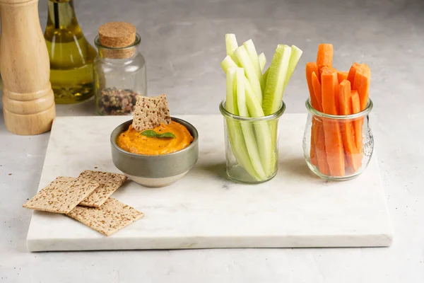 Kırmızı biber sosu portakallı kabak püresi gibi görünüyor, susam tohumlu ince krakerler, uzun şeritler ve mermer tahta üzerinde çubuklarla kesilmiş havuç ve salatalık.