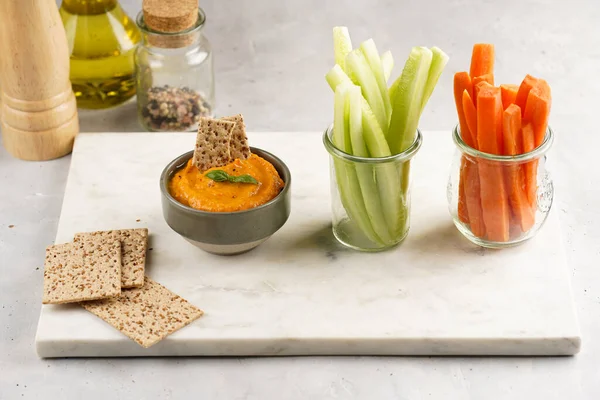 Kırmızı biber sosu portakallı kabak püresi gibi görünüyor, susam tohumlu ince krakerler, uzun şeritler ve mermer tahta üzerinde çubuklarla kesilmiş havuç ve salatalık.