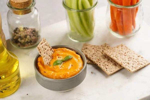 Kırmızı biber sosu portakallı kabak püresi gibi görünüyor, susam tohumlu ince krakerler, uzun şeritler ve mermer tahta üzerinde çubuklarla kesilmiş havuç ve salatalık.