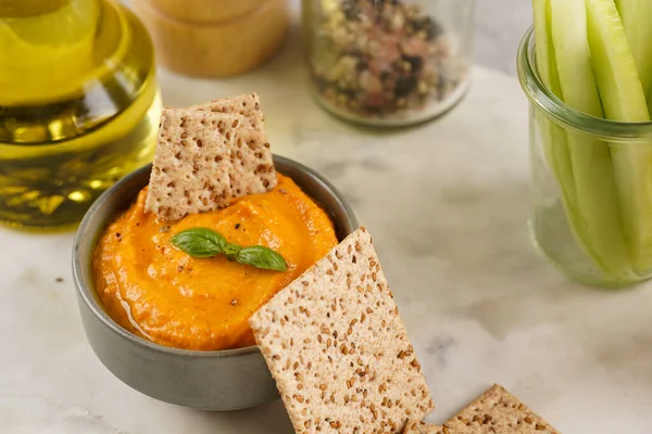 Kırmızı biber sosu portakallı kabak püresi gibi görünüyor, susam tohumlu ince krakerler, uzun şeritler ve mermer tahta üzerinde çubuklarla kesilmiş havuç ve salatalık.