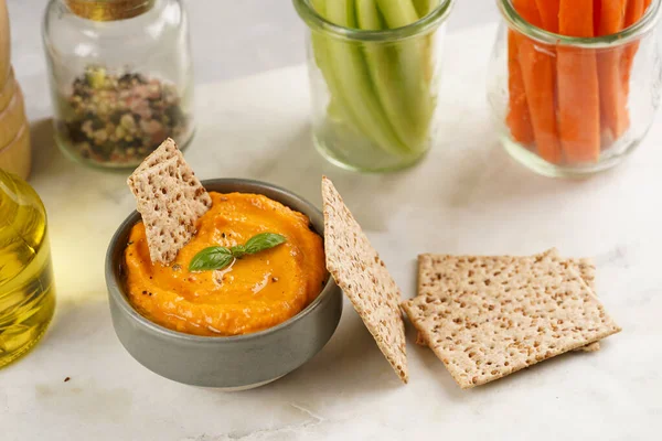 Kırmızı biber sosu portakallı kabak püresi gibi görünüyor, susam tohumlu ince krakerler, uzun şeritler ve mermer tahta üzerinde çubuklarla kesilmiş havuç ve salatalık.
