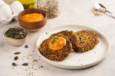 Paprika humusuyla kaplı bir tabakta havuç ve kinoa krepleri, ayçiçeği çekirdekleri. Sağlıklı vejetaryen yiyecekler - bitki temelli diyet kavramı.