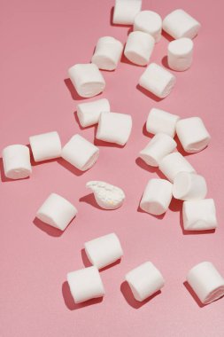 Pembe bir yüzeye serpilmiş sert ışıkta yumuşak beyaz şekerlemeler.