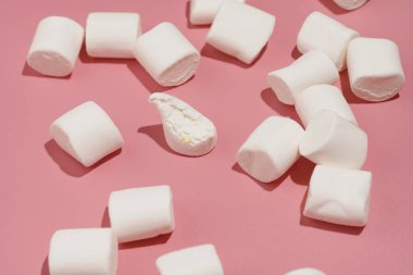 Pembe bir yüzeye serpilmiş sert ışıkta yumuşak beyaz şekerlemeler.