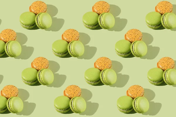 Hard light pattern of a macaron pastry - two green ones and one orange - photographed on light green surface