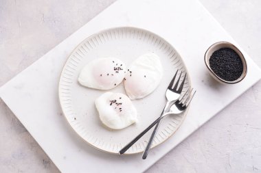 Yumurta sarısı ve siyah susam tohumlu üç haşlanmış yumurta mermer bir levhada beyaz bir tabakta ve gümüş çatallarda