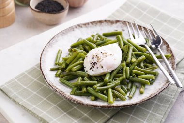 Pişmiş yeşil fasulyeli ve yeşil kareli mutfak havlusunda kahverengi kenarlı yumuşak haşlanmış susam tohumlu yumurta.