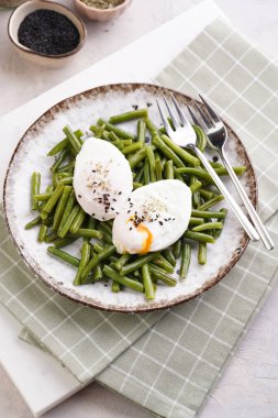 Pişmiş yeşil fasulyeli ve yeşil kareli mutfak havlusunda kahverengi kenarlı yumuşak haşlanmış susam tohumlu yumurta.