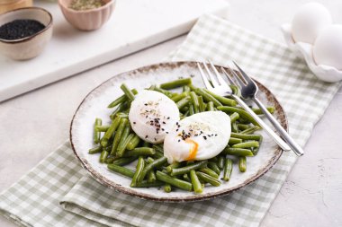 Pişmiş yeşil fasulyeli ve yeşil kareli mutfak havlusunda kahverengi kenarlı yumuşak haşlanmış susam tohumlu yumurta.