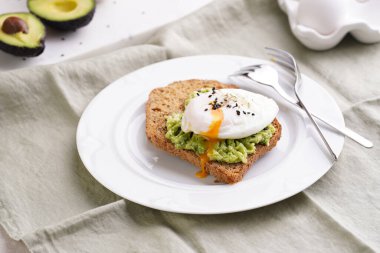 Glütensiz ayçiçeği tohumlu ekmek, haşlanmış avokado, haşlanmış yumurta ve yeşil peçetedeki beyaz tabakta susam tohumları.