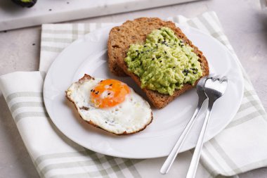 Glütensiz ayçekirdeği dilimleri. Avokado püresi, sahanda yumurta ve yeşil peçetedeki beyaz tabakta susam tohumu.