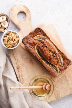 Tahtada cevizli çikolatalı muz ekmeği ve gri tarafsız arka planda malzemeler.