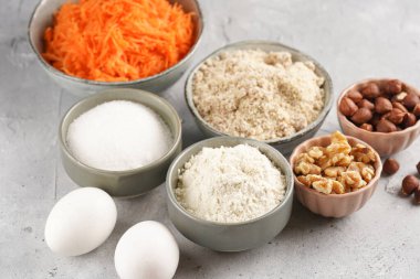 Havuçlu kek pişirmek için malzemeler: ince rendelenmiş havuç, yer fıstığı ve badem, doğranmış ceviz, beyaz un, yumurta, gri zemin üzerinde şeker