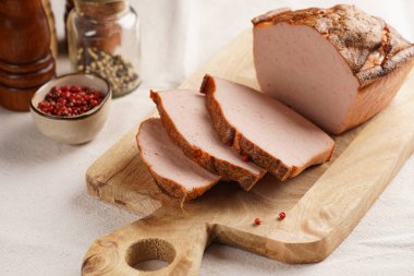 Geleneksel fırın fırınlanmış Bavyera yemeği leberkaese dilimi - konserve sığır eti, domuz eti ve pastırmadan yapılmış et yemeği, iyi öğütülmüş ekmek somunu olarak pişiriliyor, bej renkli masa örtüsü üzerinde ahşap bir tahta üzerinde