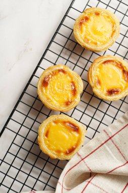 Geleneksel Portekiz vanilyalı puding puf puf pastası siyah fırın rafında mermer arka planda kareli mutfak havlusu