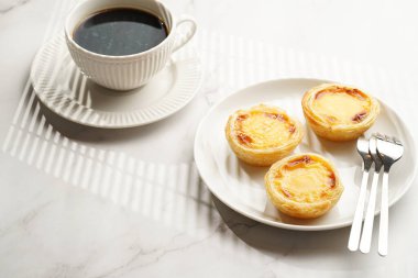 Geleneksel Portekiz pudingi puding puf böreği pastel de nata siyah fırın rafında beyaz tabakta beyaz porselende bir fincan kahveyle