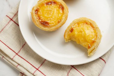 Geleneksel Portekiz vantugulü puding puf böreği pastalı nata beyaz tabakta kareli mutfak havlusunda beyaz porselenli bir fincan kahve, üst manzara