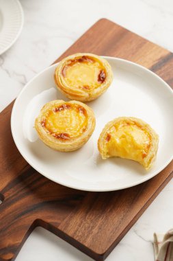 Geleneksel Portekiz pudingi puding puf böreği pastel de nata beyaz tabakta tahta tahtada beyaz porselende bir fincan kahveyle birlikte