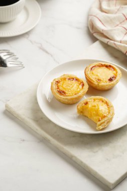 Geleneksel porselen porselen bir fincan kahveyle mermer tahtada beyaz tabakta geleneksel Portekiz vanilyalı puding puf böreği pastel de nata.
