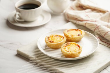 Geleneksel porselen porselen bir fincan kahveyle mermer tahtada beyaz tabakta geleneksel Portekiz vanilyalı puding puf böreği pastel de nata.