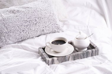 beyaz porselen bir fincan siyah kahve americano ve gri mermer tepside çay tabağı bembeyaz yastıklar arasında beyaz yatak çarşafları - yatakta kahvaltı