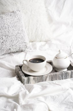beyaz porselen bir fincan siyah kahve americano ve gri mermer tepside çay tabağı bembeyaz yastıklar arasında beyaz yatak çarşafları - yatakta kahvaltı