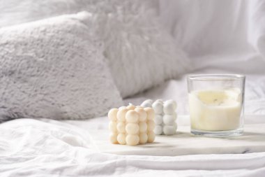 Üç mum - cam kavanozda baloncuk mumları ve gümüş kapaklı beyaz yastıklı mermer tablet