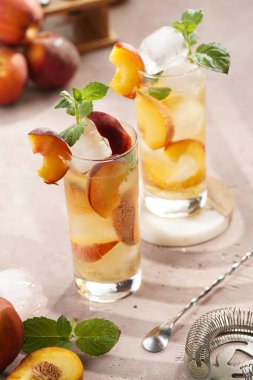 Buzlu, şeftali dilimli ve soluk mor arkaplanlı taze naneli ferahlatıcı yaz kokteyli.