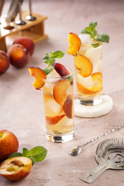 Buzlu, şeftali dilimli ve soluk mor arkaplanlı taze naneli ferahlatıcı yaz kokteyli.