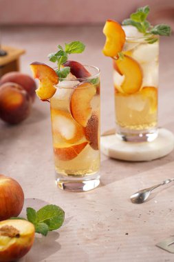 Buzlu, şeftali dilimli ve soluk mor arkaplanlı taze naneli ferahlatıcı yaz kokteyli.