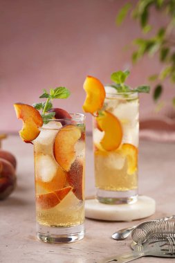 Buzlu, şeftali dilimli ve açık mor arkaplanlı taze naneli ferahlatıcı bir kokteyl.