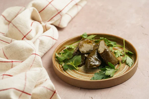 Traditional middle east stuffed vegetable dish dolma - rice wrapped in grape leaves with fresh parsley branches and coriander on round brown plate