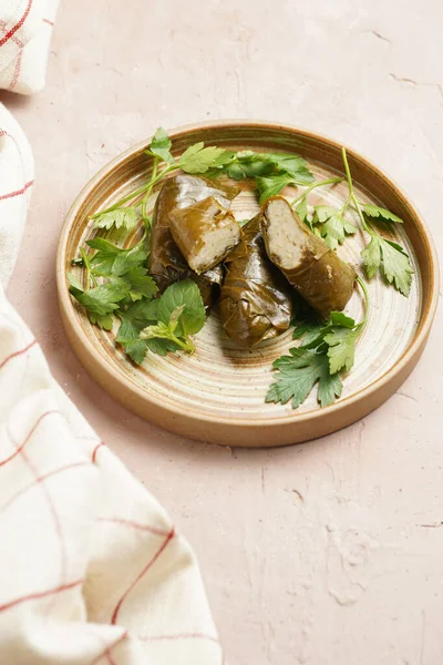 Traditional middle east stuffed vegetable dish dolma - rice wrapped in grape leaves with fresh parsley branches and coriander on round brown plate