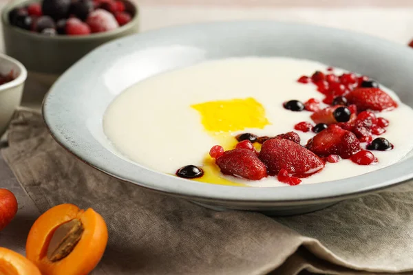 Traditional breakfast semolina porridge - creamy pudding with butter, frozen berries and fresh apricots in a grey plate